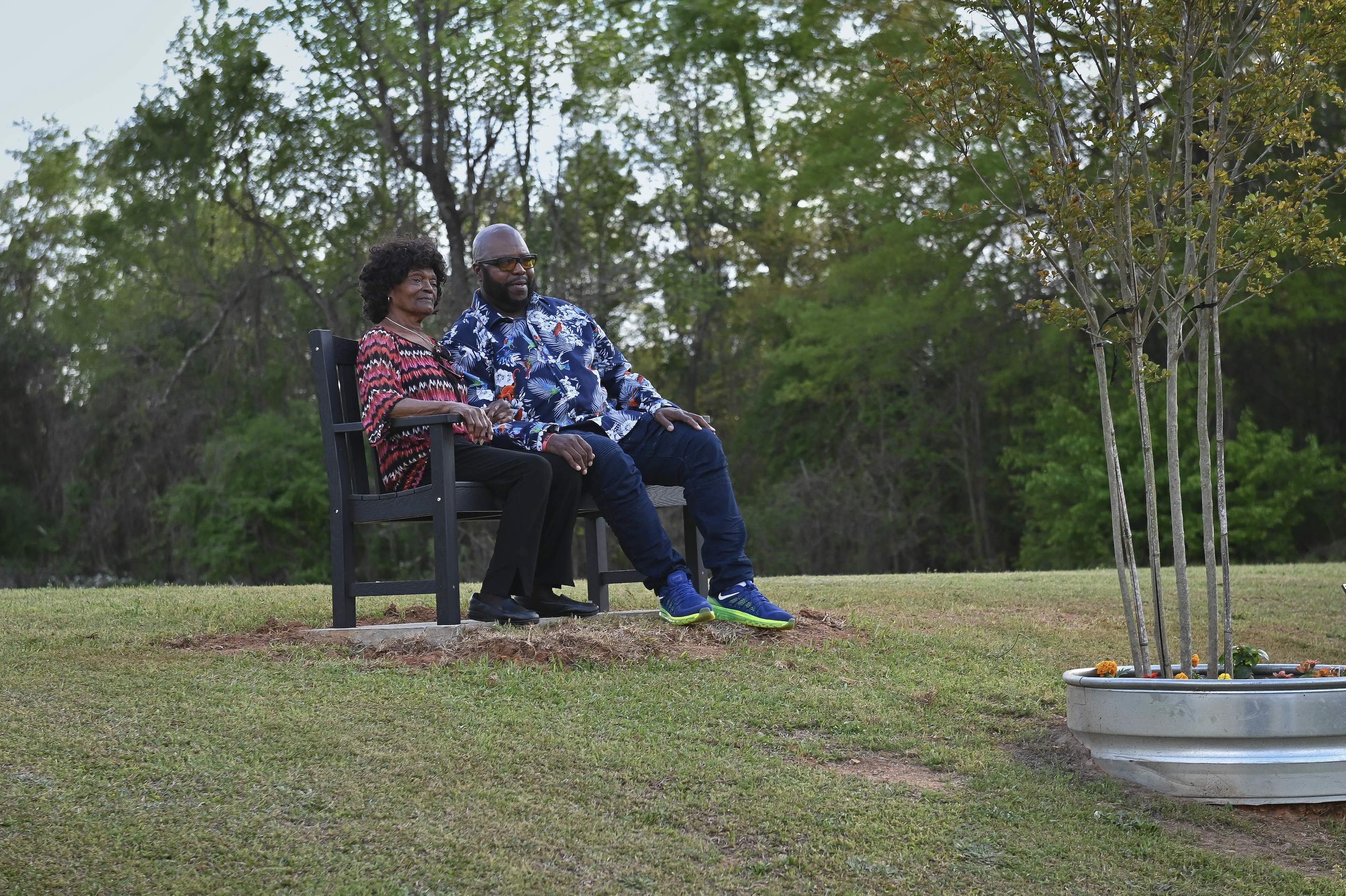 Gladys, wife of the late Deacon Joseph Ward Sr., sit with her son on a memorial bench in honor of her husband at Collins P. Lee Community Center.