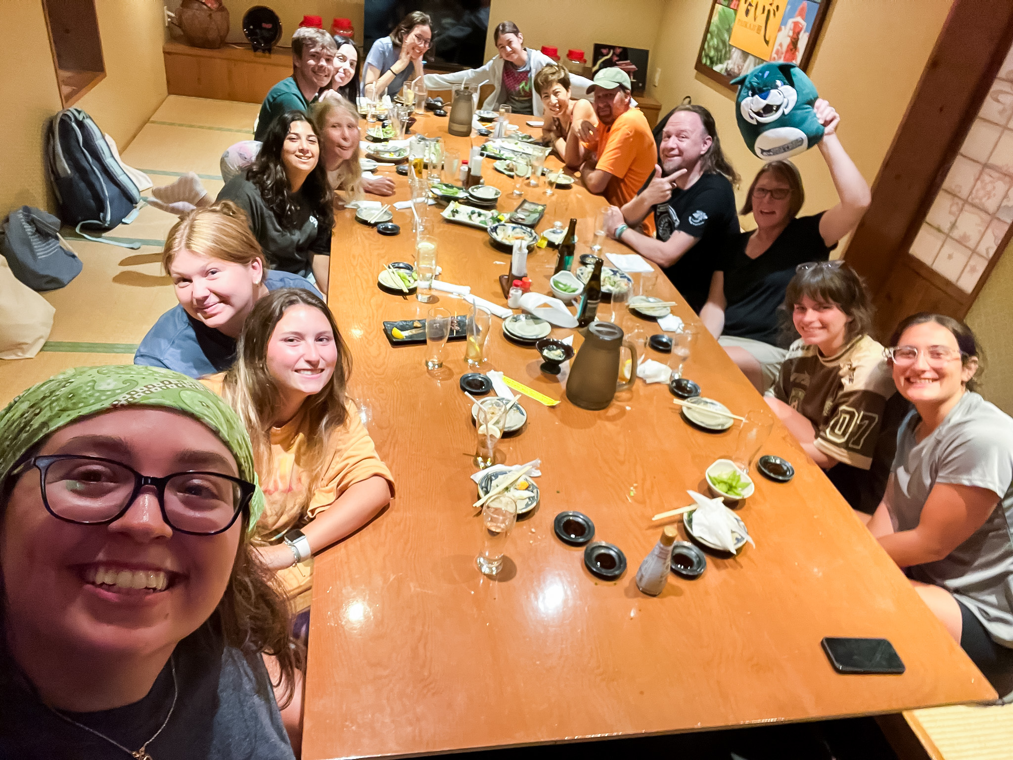 Students lean in for a photo around a wide table in a private izakaya room.