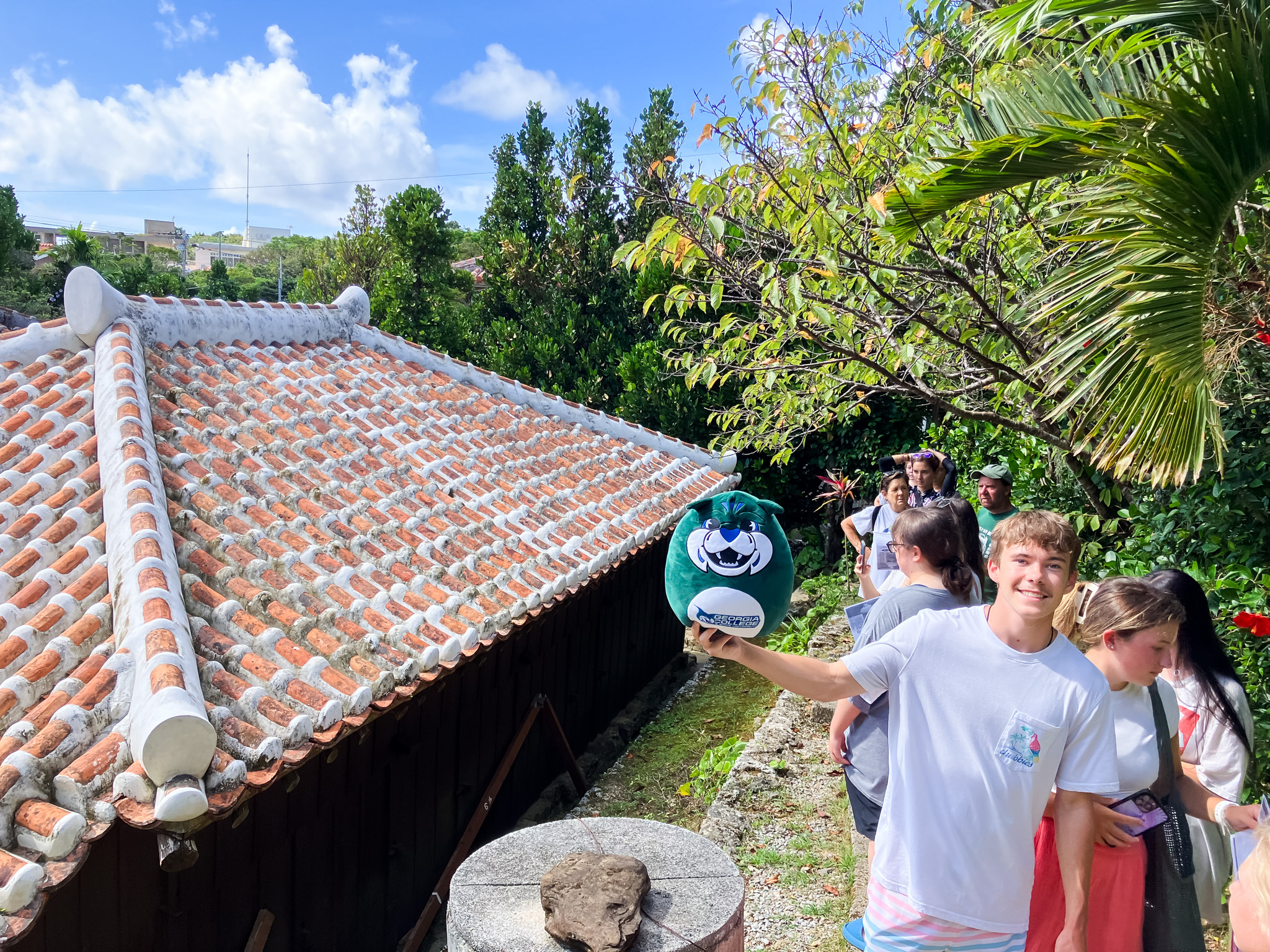 A male student lifts lil' Thunder up in front of the roof of Nakamura House.