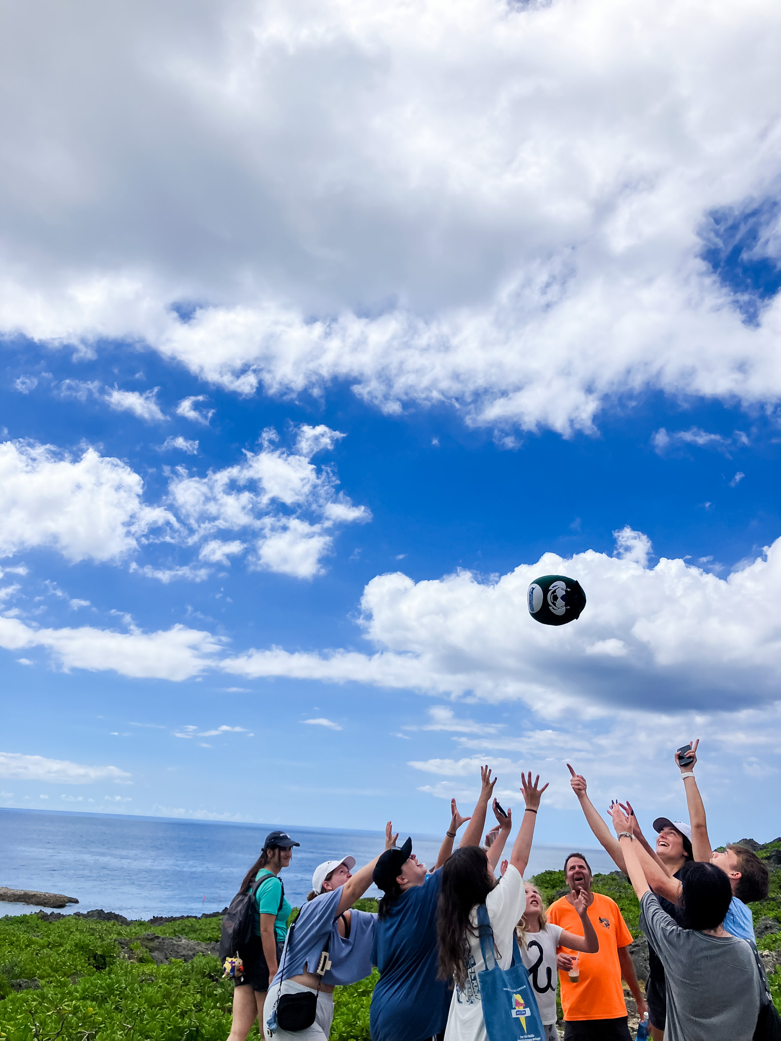 The group of students, with the sea in the background, throw lil' Thunder into the air.