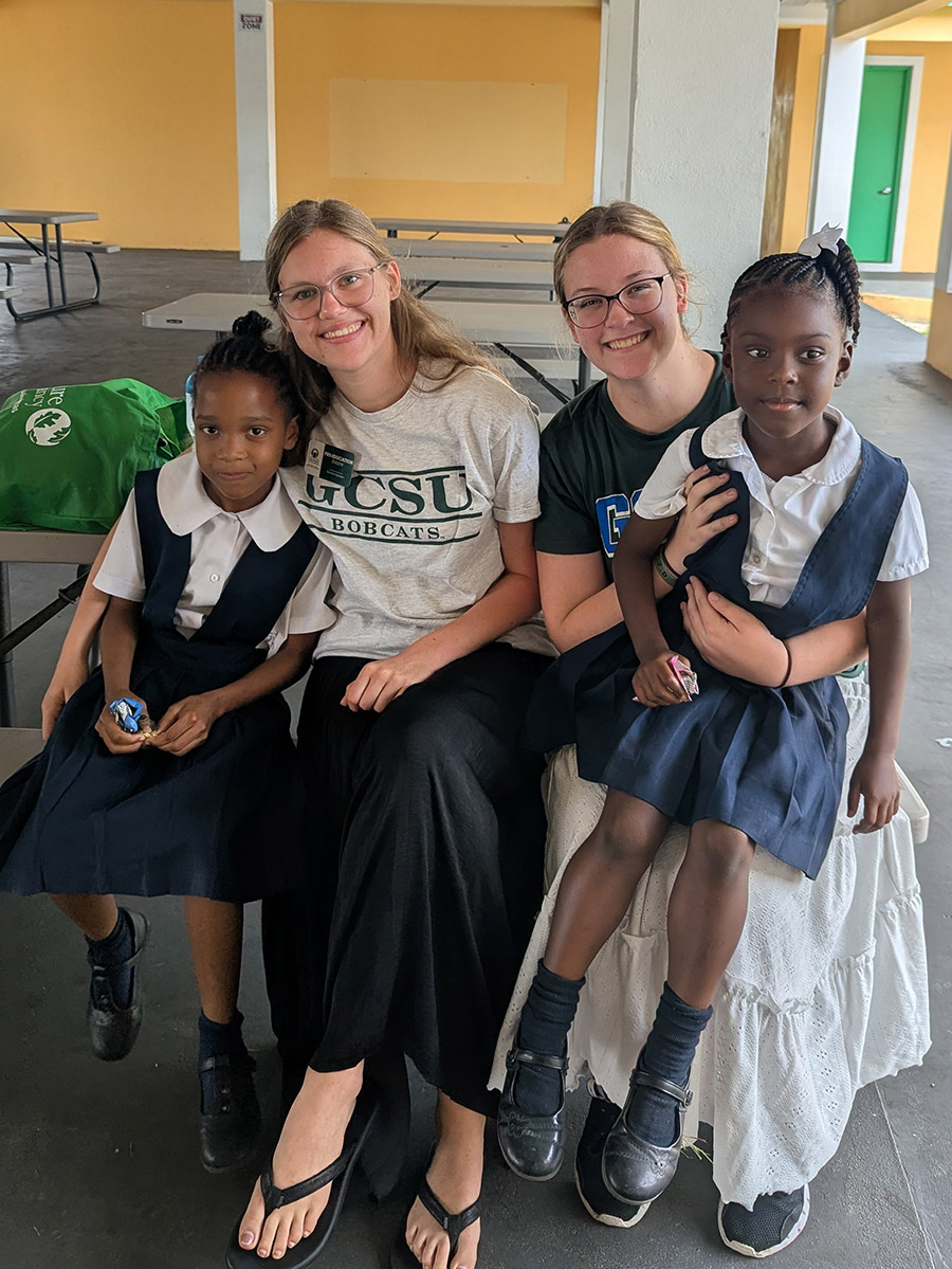 Addison Rathbun, left, and Brooke Kersey enjoy a break with Bahamian elementary students. (Photo: Miriam Jordan)