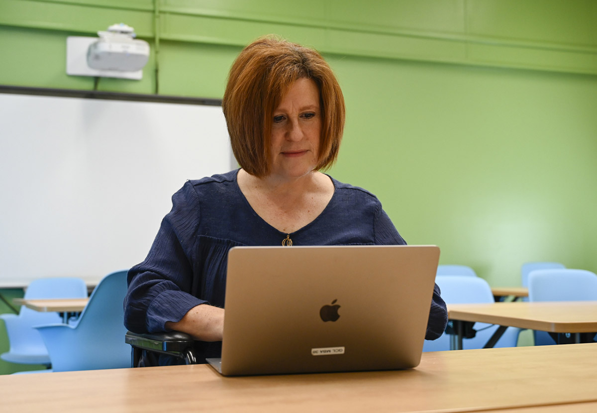 Dr. Cynthia Alby is seated working on a Mac laptop