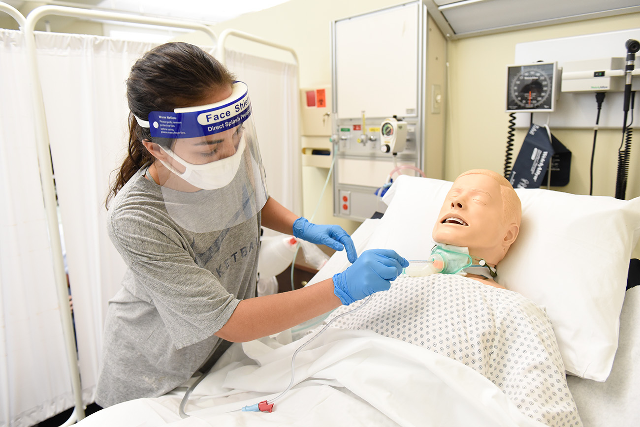 A student nurse trains with a medical manikin in PPE gear. 